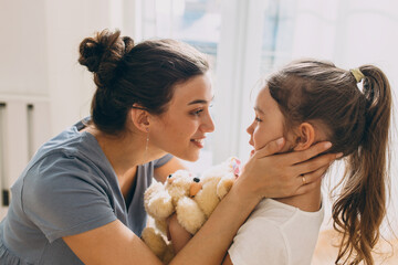 Adorable charming mom of 20s with cute hair bun dressed in grey casual summer dress cuddling with...