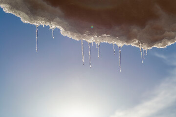 melting icicles with the blue sky and sun in the background. Spring weather with thawing ice