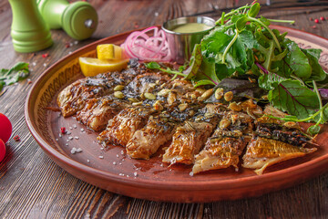 Grilled baked mackerel served with sauce, onion, lemon and green salad on wooden table