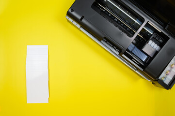 Top view of photo printer and blank sheets of photo paper on yellow background