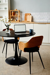 Vertical background image of minimal home workplace with open laptop on black kitchen table and elegant wooden chairs, copy space