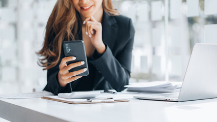Young businesswoman looking at financial information from a mobile phone, she is checking company financial documents, she is a female executive of a startup company. Concept of financial management.