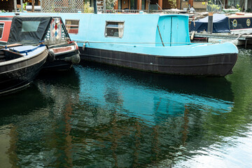 Fototapeta na wymiar Boats along a London canal that are reflected in the water of the river, dominance of blue and green colors.
