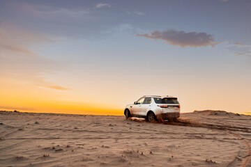 Fototapeta na wymiar White SUV in the desert at sunset. Off road Test drive. A car in the desert quickly rides through the mud with clouds of dust from under the wheels