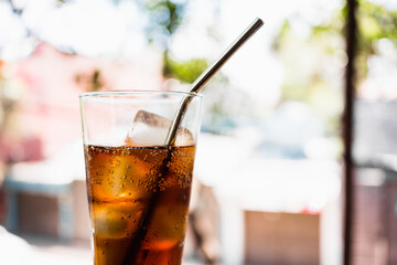 Cola drink with ice and aluminum straw with the street in the background.