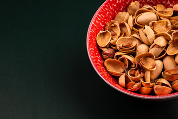 View from above of organic pistachio shells in a red cup sitting on a green table. Concept of health. Copy space.  