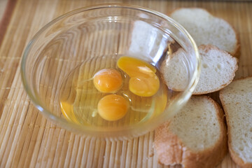 Three raw eggs in a clear glass bowl on the kitchen table with white bread. Step-by-step cooking of eggs for breakfast. High quality photo