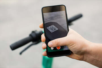 Hand of unrecognizable man using smartphone for renting modern electric scooter with an...