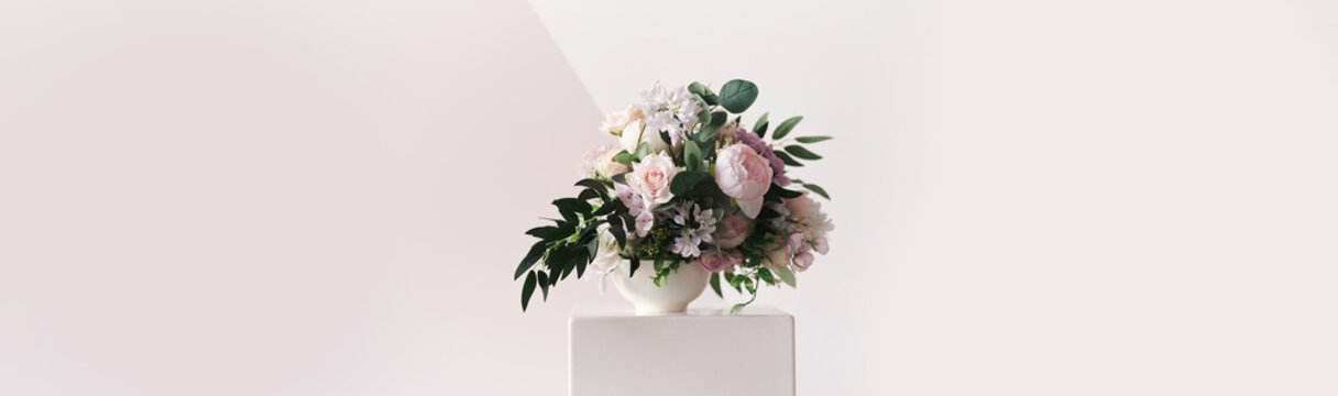 The banner is a composition of different colors in a white vase standing on a podium. Against the background of a geometrically painted wall. A beautiful freshly cut bouquet. High quality photo
