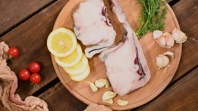 Raw fish cod on a tray, lemon tomato and pepper, wooden table in rustic style rotation. High quality 4k footage
