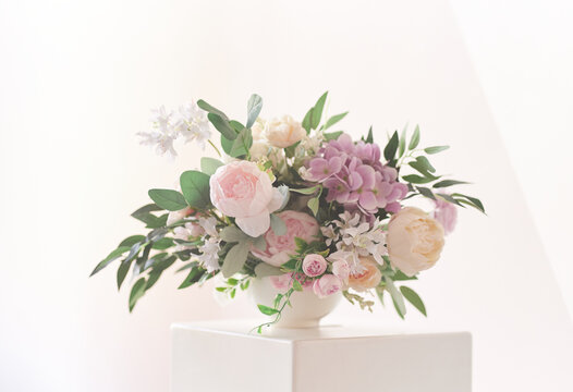A composition of different flowers in a white vase on a square podium. The concept of a flower shop. A beautiful freshly cut bouquet. Flower delivery. High quality photo