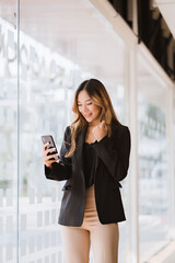 Fototapeta premium Asian businesswoman in formal suit in office happy and cheerful during using smartphone and working