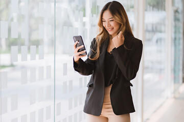 Fototapeta na wymiar Asian businesswoman in formal suit in office happy and cheerful during using smartphone and working