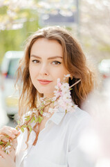 girl in a white shirt with a branch of sakura in the spring