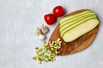 Sliced courgette vegetables on a wooden cutting board, tomatoes and garlic