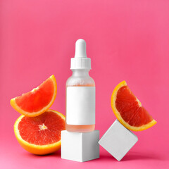Cosmetic bottle with a pipette on a white podium, next to a cut red orange, on a pink background....