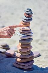 Fototapeta na wymiar A woman's hand points or pushes a tall cairn on a sandy beach