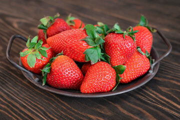Close-up fresh strawberries at steel tray on wooden table. Tray with whole ripe strawberries