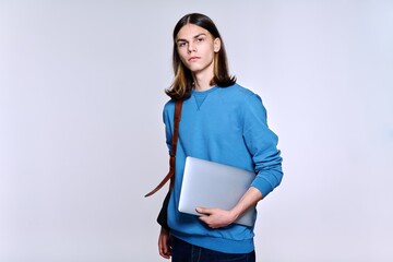 Portrait of serious student guy with backpack laptop looking at camera, light studio background