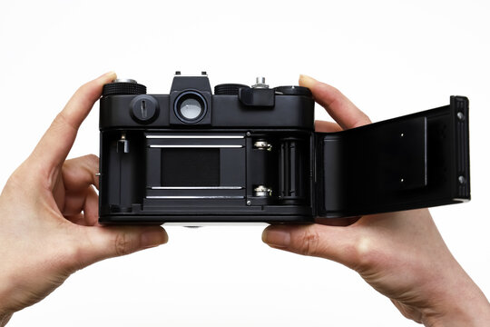 Old Camera With An Open Back Door Holding Two Hands On A White Background. Shallow Depth Of Field