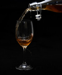 A glass and spilling wine from a bottle on a black background. Close-up