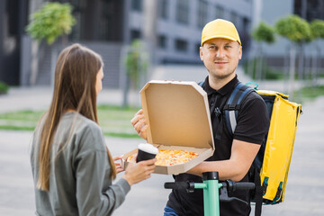 Attractive young man courier with yellow thermal backpack delivering pizza box and cup of coffee to caucasian girl customer. Delivery man holding cardboard box and cup with hot drink