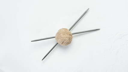 a ball of beige yarn for knitting pierced with knitting needles lies on a light background in the middle. close-up