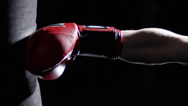 Fighter Practicing Some Kicks With Punching Bag - A Man With A Tattoo Boxing On dark Background. Kick, punching bag on dark background. Black punching bag weighs at the gym