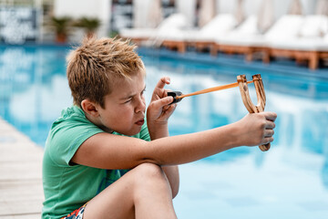 A boy shoots a slingshot near the pool