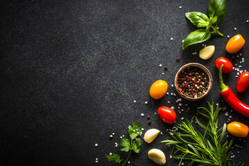 Food cooking background on black stone table. Fresh vegetables, herbs and spices. Ingredients for cooking with copy space.