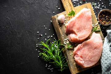 Turkey steaks with spices and herbs at craft cutting board at black stone table. Top view with copy space.