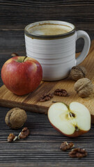 walnuts, apples and a clay mug with a drink stands on a wooden background
