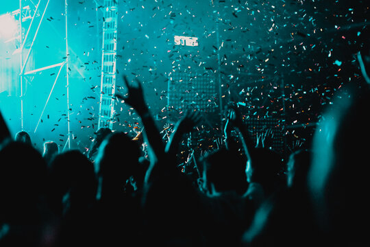 cheering crowd with raised hands and falling confetti at concert - music festival