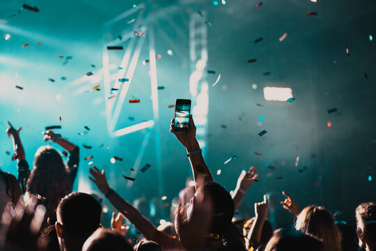 cheering crowd with raised hands and falling confetti at concert - music festival