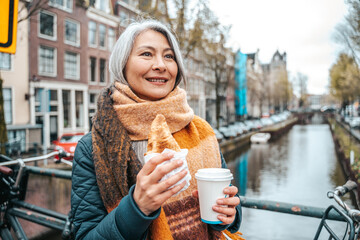 Senior woman have a breakfast in amsterdam with coffee and croissant - obrazy, fototapety, plakaty
