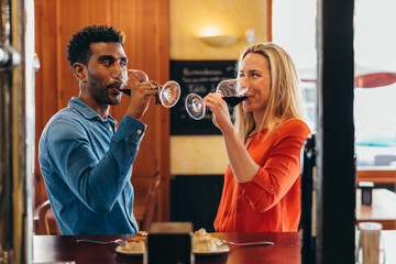 multiethnic couple look at each other with feeling while drinking red wine from their glasses