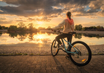 Woman riding a mountain bike near lake at sunset in summer. Colorful landscape with sporty girl...