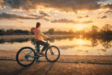 Woman riding a mountain bike near lake at sunset in summer. Colorful landscape with sporty girl...