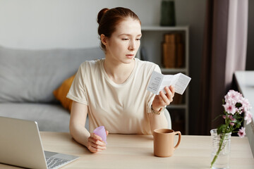 Portrait of Caucasian young woman reading instruction manual for menstrual cup at home in minimal...
