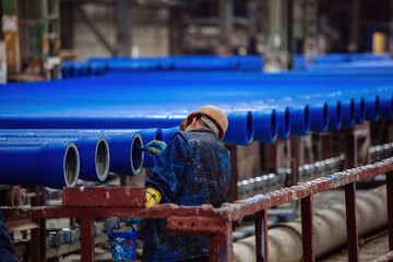 Worker painting new cast iron pipes in blue color