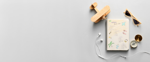 Notebook with travel check-list, toy airplane, compass, sunglasses and earphones on light...