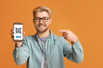 Handsome man pointing at smartphone with QR code on screen against orange background
