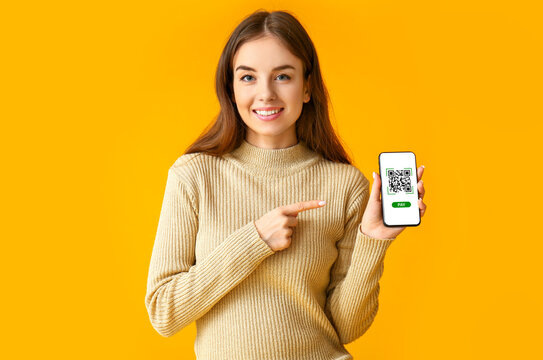 Beautiful young woman holding smartphone with QR code on screen against orange background