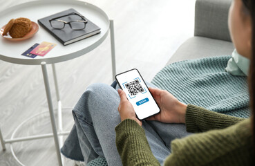 Young woman with smartphone scanning QR code at home