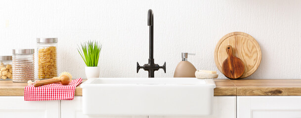Counter with modern sink, different utensils and products near white wall in kitchen. Banner for design