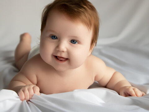 Just beautiful. Cute smiling baby. Cute 3 month old Baby girl infant on a bed on her belly with head up looking with her big eyes. Natural bedroom light. Infant baby. Healthy and medical concept