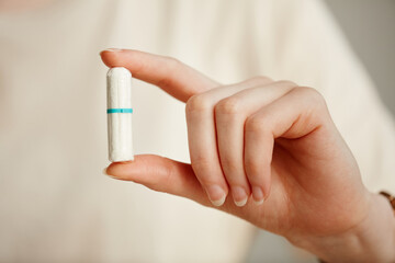 Minimal closeup of young woman holding tampon between two fingers showing it to camera, copy space