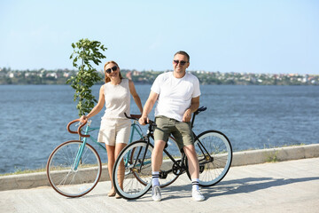 Mature couple with bicycles walking along river bank on summer day