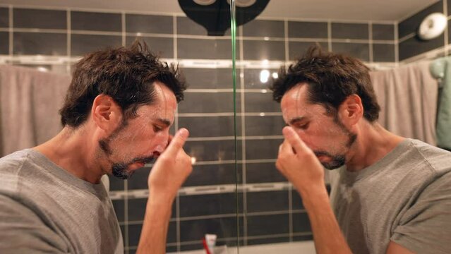 Person washing face in front of bathroom mirror man using facial cleanser at night routine