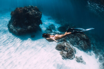 Woman freediver in bikini dive on sandy bottom with corals. Attractive slim girl with fins...